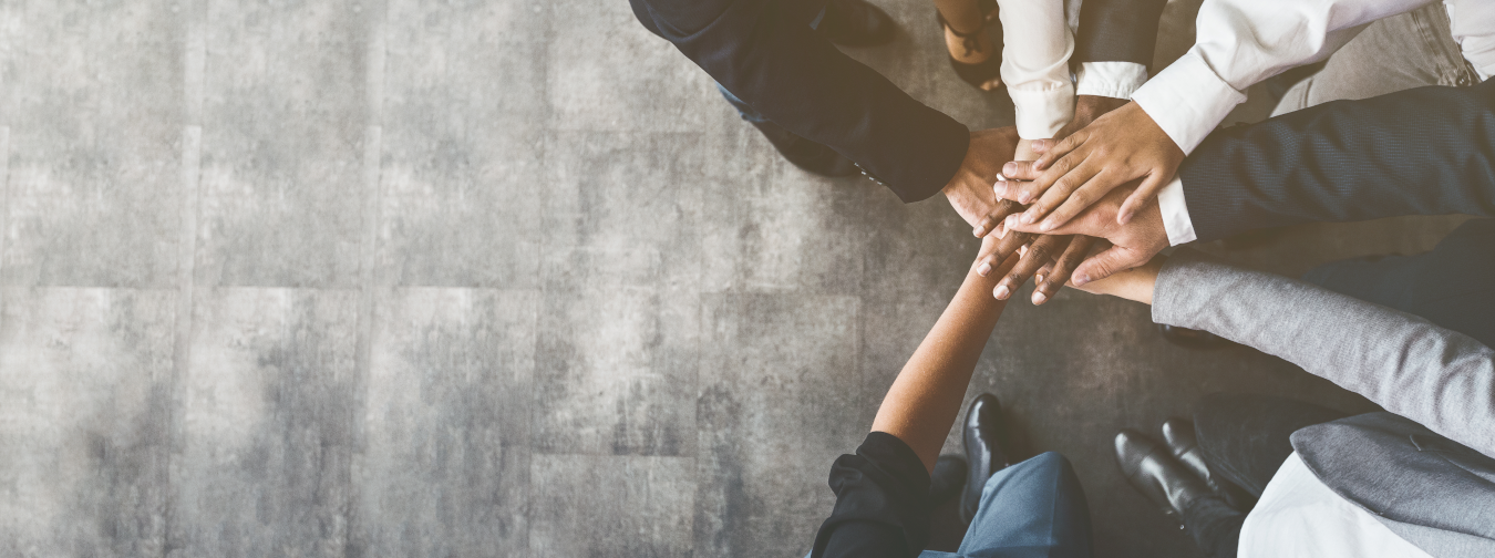 Mehrere Personen legen ihre Hände übereinander zu einem Stapel. Die Szene wird von oben fotografiert. Es handelt sich um ein Symbol für Teamarbeit oder Zusammenhalt.
